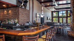 Un espace bar doté d’un long comptoir, de nombreux tabourets et d’un mur en briques en arrière-plan.