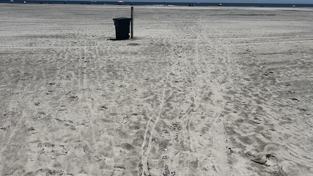 A wide, open sandy beach with a single trash bin in the center.