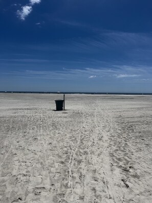 Une vaste plage de sable, ouverte et dégagée, avec une seule poubelle au centre.
