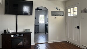 A living room with a flat-screen TV mounted on the wall, a dark wooden entertainment center, and a hallway leading to a kitchen.