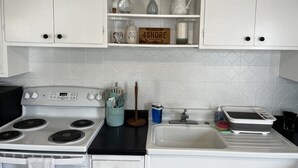 A kitchen with white cabinets, a stove, a sink, and various kitchen items on the countertop.