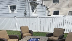 An outdoor patio area with wicker furniture and a square table with a built-in fire pit.
