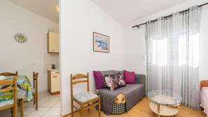 En kompakt opholdsstue med et tekøkken, en sofa med puder, et glasbord og en seng.