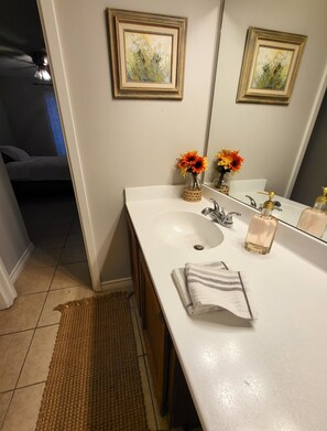 A bathroom with a white sink, two framed floral paintings, a mirror, and a small vase with orange flowers.