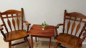 Two wooden chairs with curved backs and turned legs, a small square table with a green plant, and a white textured wall.