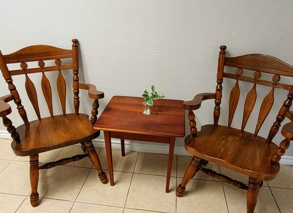 Two wooden chairs with curved backs and turned legs, a small square table with a green plant, and a white textured wall.