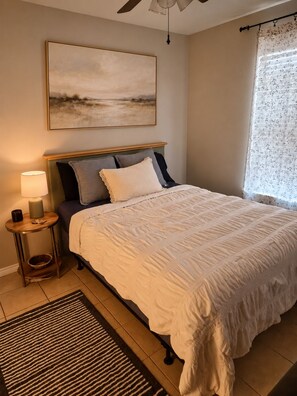A bedroom with a bed, bedside table, lamp, and a painting on the wall.