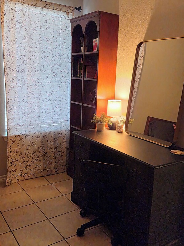 A bathroom with a vanity, a mirror, a cabinet with books, and a potted plant.