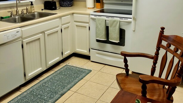 A kitchen with white cabinets, a stove, a microwave, a sink, and a dining table with a chair.