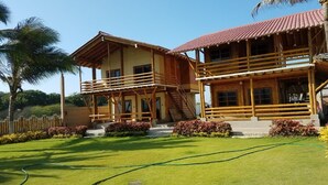 A two-story wooden house with a balcony, a staircase, and a well-maintained lawn. - Cabins in front of the Beach -  Playas - Ecuador (Playas)