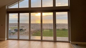 Un'ampia stanza con vista sulla spiaggia e sul tramonto attraverso delle vetrate a tutta altezza.