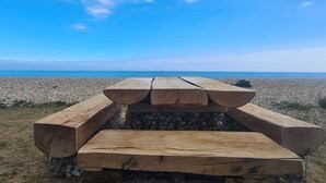 Un tavolo da picnic in legno con panche, su una spiaggia di ciottoli sotto un cielo sereno.