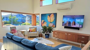 A modern living room with a blue sofa, a small table, a chair, a TV, and a potted plant. - Goldfinch House - Scandinavian Modern Near Beaches (Seattle)