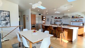 A modern kitchen with a central island, stainless steel appliances, and a dining area with a white table and chairs. - Goldfinch House - Scandinavian Modern Near Beaches (Seattle)
