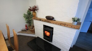 A fireplace with a white brick surround, a wooden mantel, and a black hearth. There are two wooden chairs and a small table in front. - Lymm Cottage (Lymm)