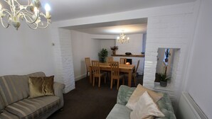 A living room with a sofa, a dining table with chairs, a chandelier, and a fireplace. - Lymm Cottage (Lymm)