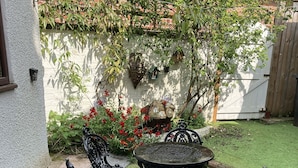 A garden patio with a table and four chairs, surrounded by a white wall and a brick building. - Lymm Cottage (Lymm)