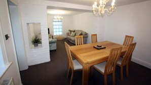 A dining area with a wooden table and chairs, a chandelier, and a sofa in the background. - Lymm Cottage (Lymm)