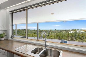 Una cocina con un amplio ventanal, un lavamanos de acero inoxidable y vistas a un paisaje verde.