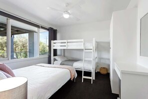 A room with a bunk bed, a single bed, a ceiling fan, and a window with curtains.