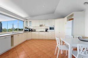 A modern kitchen with white cabinets, a dining area with white chairs, and a large window offering a view of the outdoors.