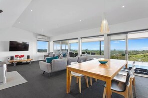 Un espacio habitable moderno con comedor, un conjunto de sofás y un amplio ventanal con vista al paisaje.
