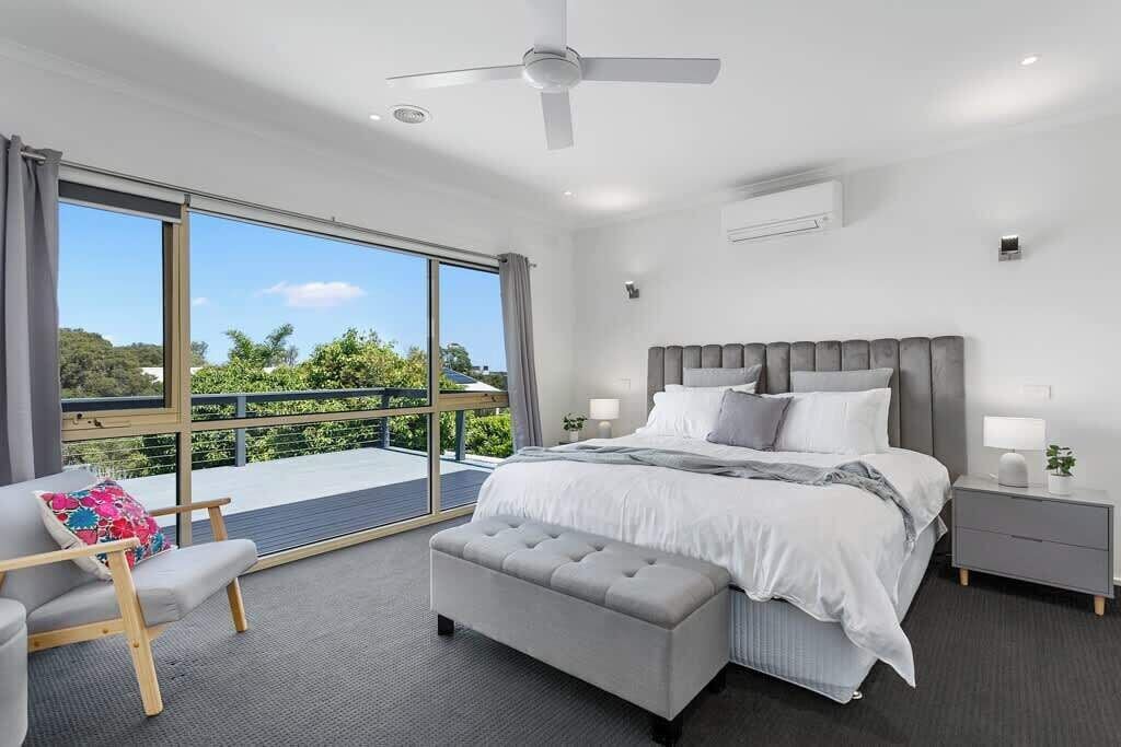 A modern bedroom with a large bed, a bedside table, a bench, and a view of the outdoors.