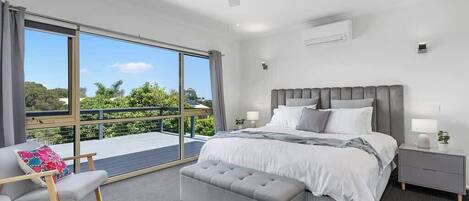 A modern bedroom with a large bed, a bedside table, a bench, and a view of the outdoors.
