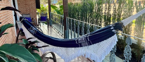 Una hamaca en un balcón con vistas a un jardín y edificios.