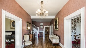 A grand hallway with a piano, a staircase, and a chandelier.