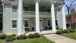 A two-story building with a central porch supported by columns, a red roof, and a well-maintained lawn.