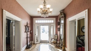 A hallway with a chandelier, a mirror, and a piano.