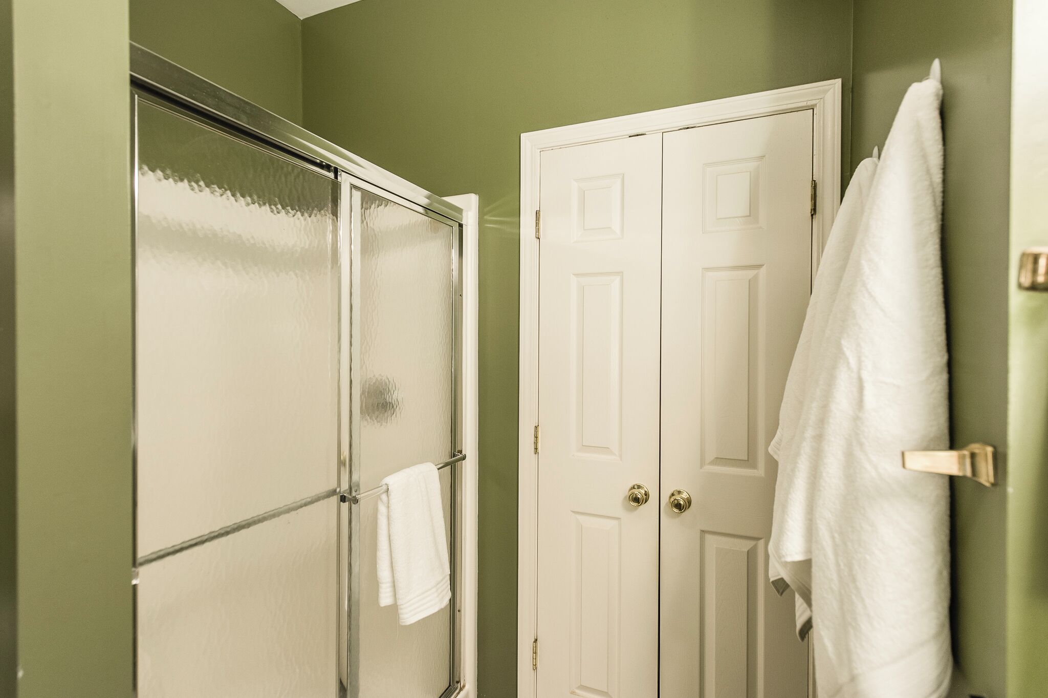 A bathroom with a glass shower door, a white door, and a towel hanging on the wall.