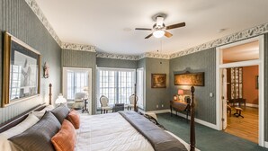 A hotel room with a large bed, a desk with a lamp, a chair, and a ceiling fan.