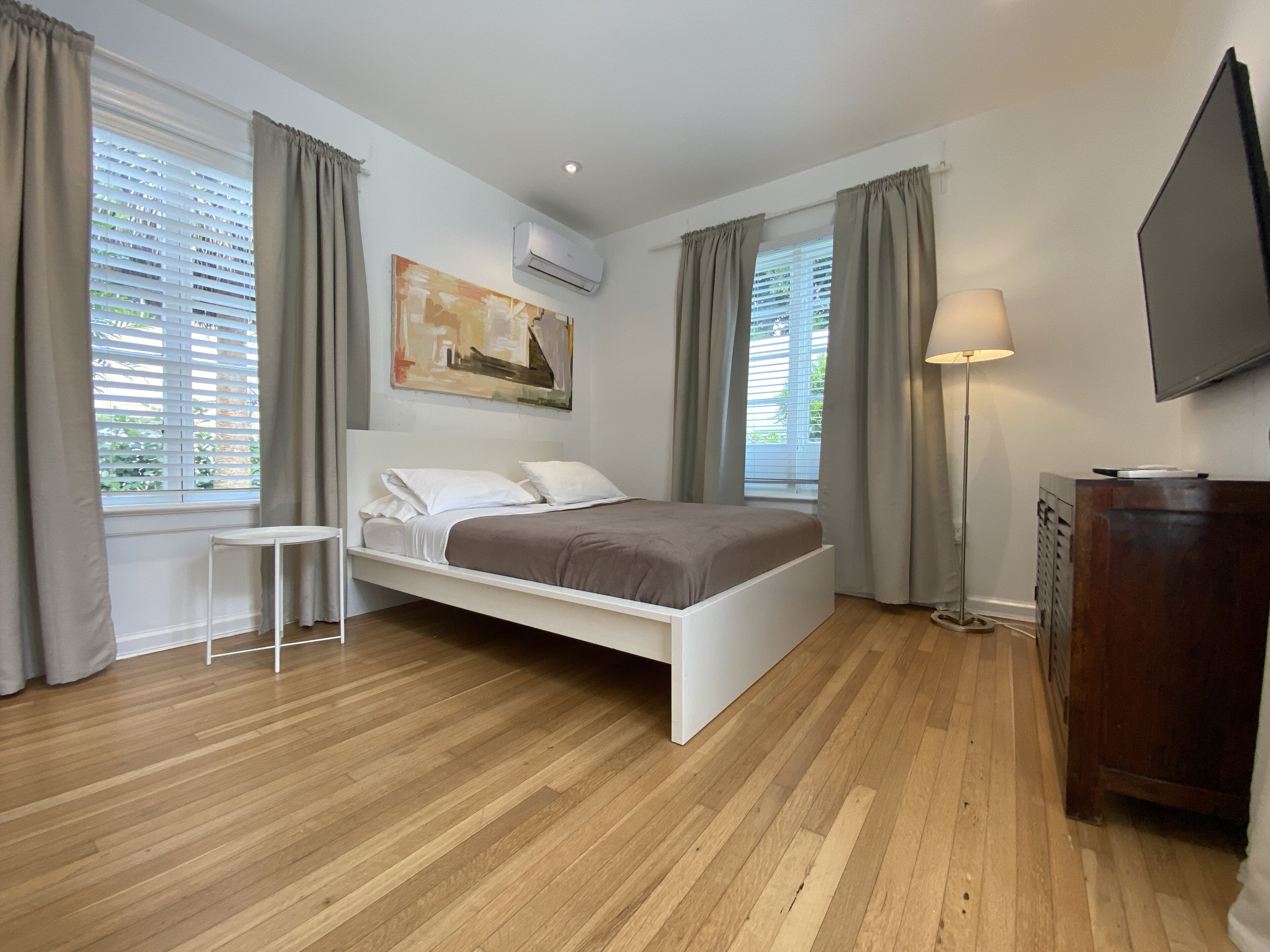A bedroom with a bed, a bedside table, a dresser, a TV, and a painting on the wall.