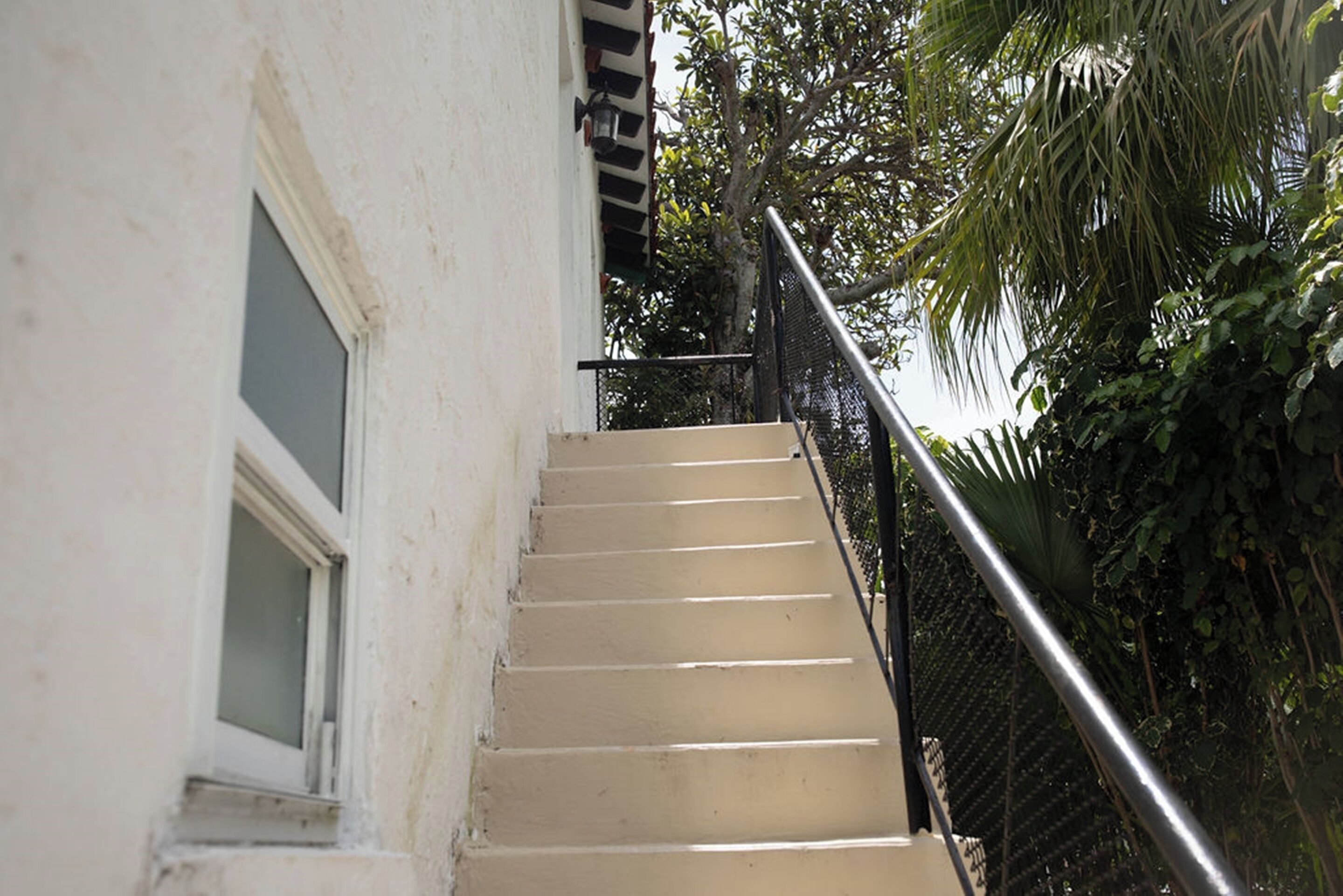 A beige staircase with a metal handrail, leading to a window with a white frame.