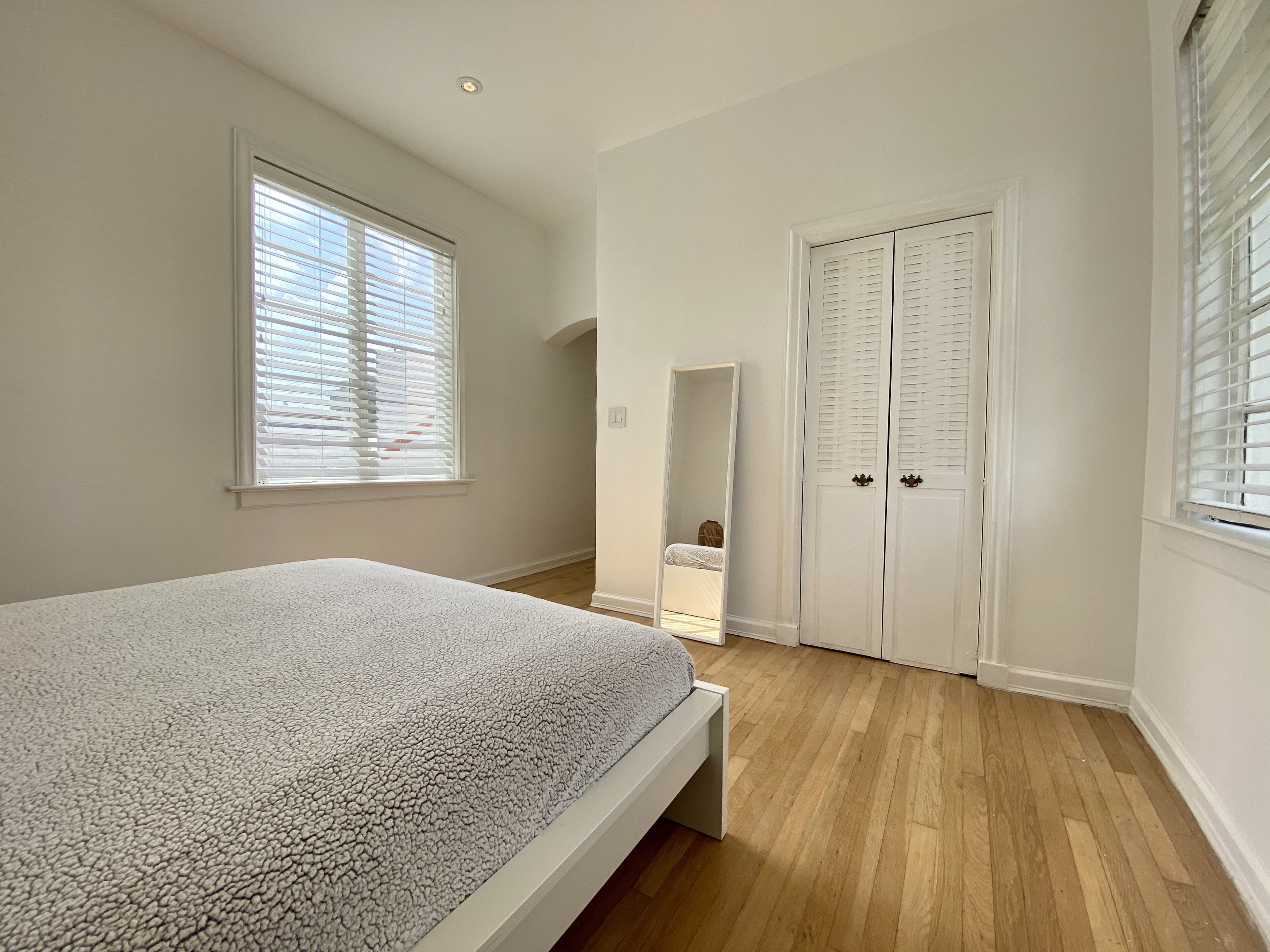 A bedroom with a bed, wooden flooring, a wardrobe, and a window with blinds.