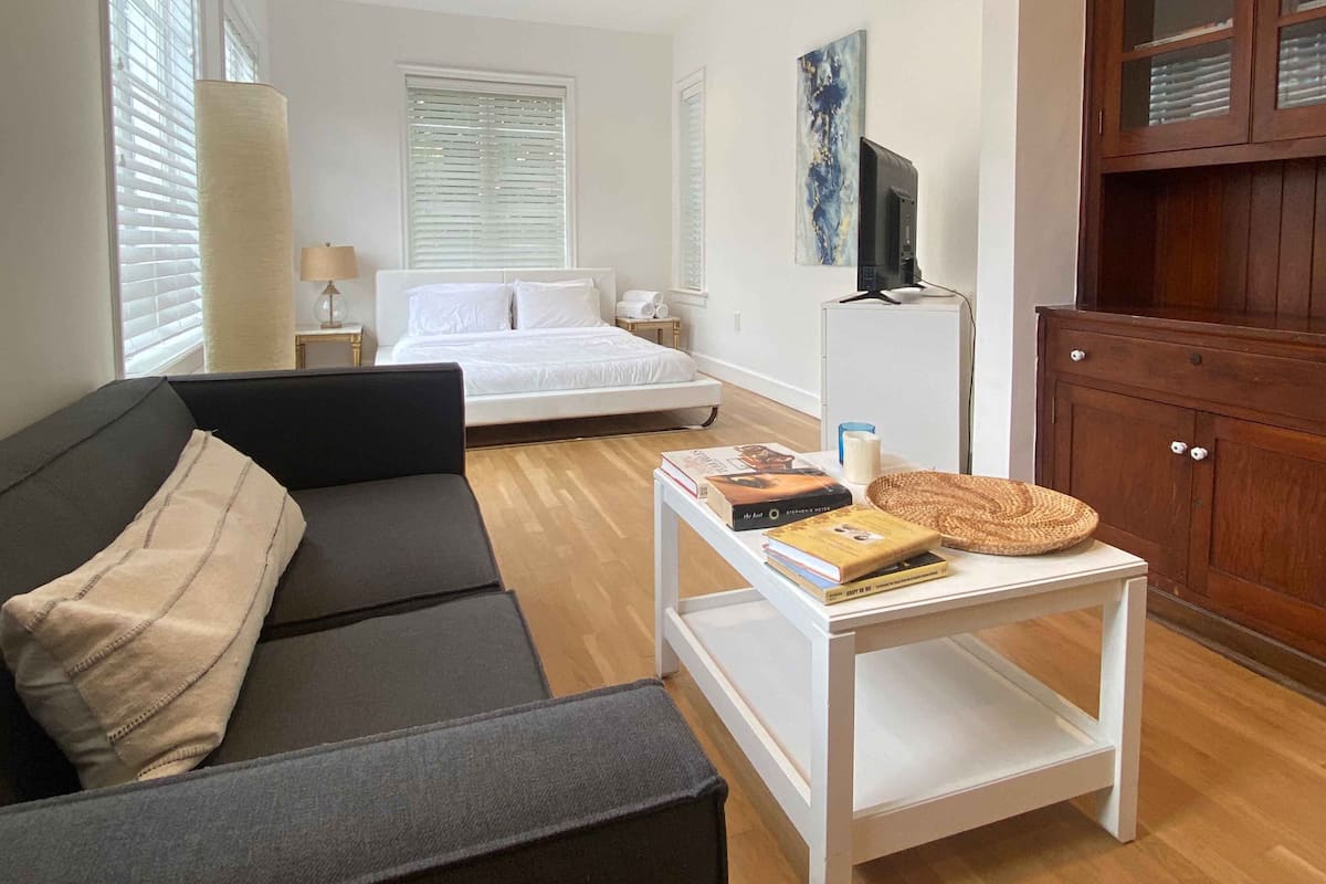 Un dormitorio con cama, una mesita de noche con libros, una lámpara y un televisor sobre un mueble.