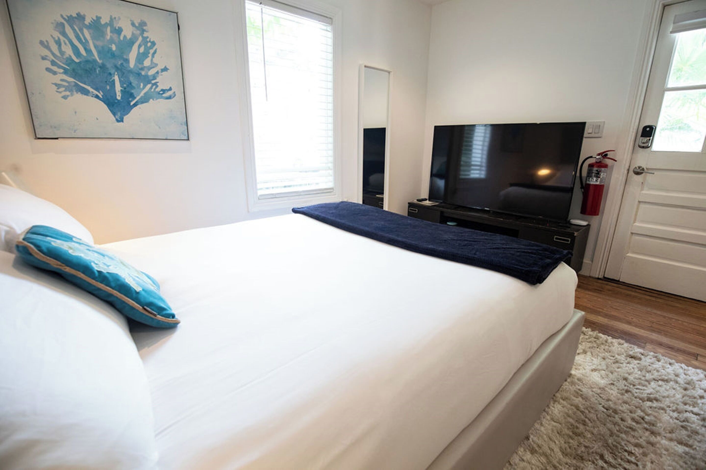 A bedroom with a bed, a television, a fire extinguisher, and a door.