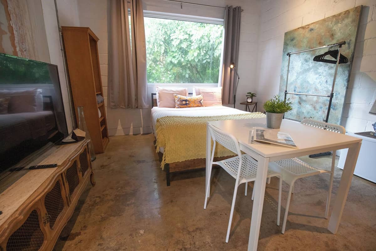 Un dormitorio con cama, escritorio, silla, televisor y ventana con cortinas.