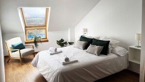 Un dormitorio con una cama grande, una silla, una mesita de noche, una lámpara y una ventana con vistas.