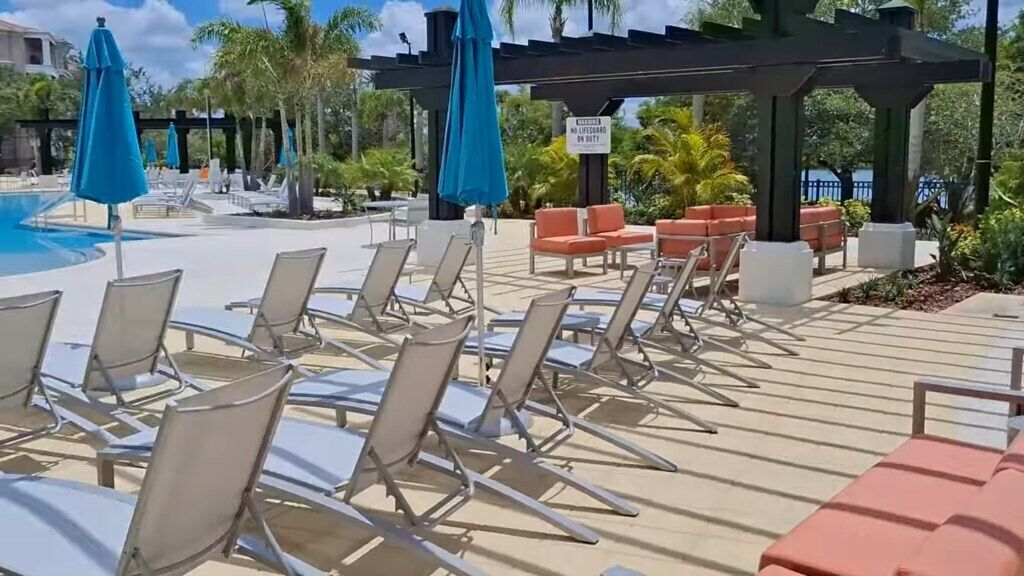 A poolside area with sun loungers and umbrellas, a covered seating area, and a sign indicating no lifeguard on duty.