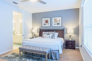 Une chambre à coucher avec un lit, des tables de chevet, un banc et un ventilateur de plafond.