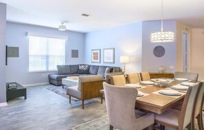 Un salon moderne comprenant un canapé, une table basse et un coin repas avec des chaises et une table dressée pour quatre personnes.