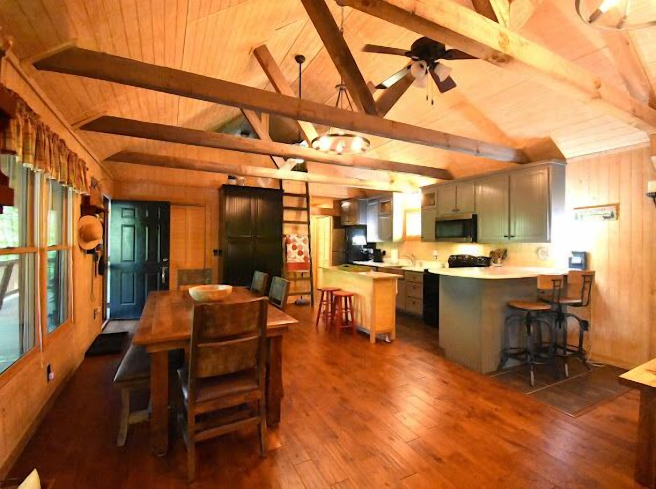 A spacious kitchen with wooden beams, a dining area with a table and chairs, and a view through a window.
