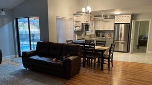 A modern living room with a dark brown sofa, a dining table with chairs, and a kitchen in the background. - Private 3Bed/3Bath Heated Pool Outdoor Entertainment (Zephyrhills)