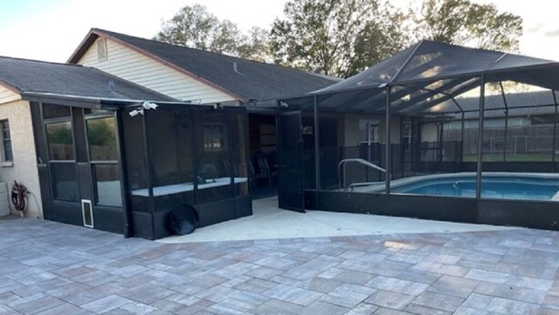 A covered outdoor area with a pool, a patio with stone tiles, and a house in the background. - Private 3Bed/3Bath Heated Pool Outdoor Entertainment (Zephyrhills)