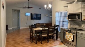 A spacious living room with a wooden floor, a dining area with a table and chairs, a kitchen with modern appliances, and a ceiling fan. - Private 3Bed/3Bath Heated Pool Outdoor Entertainment (Zephyrhills)