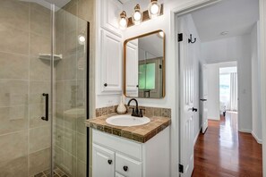 Bathroom features a glass-enclosed shower, white vanity, and a large mirror.