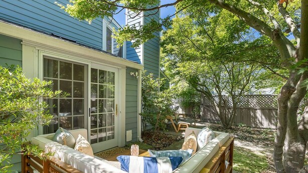 A cozy outdoor seating area with a wooden bench and cushions, a covered patio with a sliding glass door, and a wooden fence in the background. - Your escape to Napa Valley (Yountville)